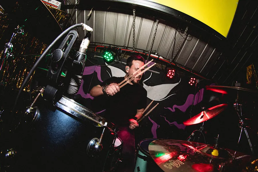 Baterista cruzando las baquetas frente a su cara, con luces verdes y rojas